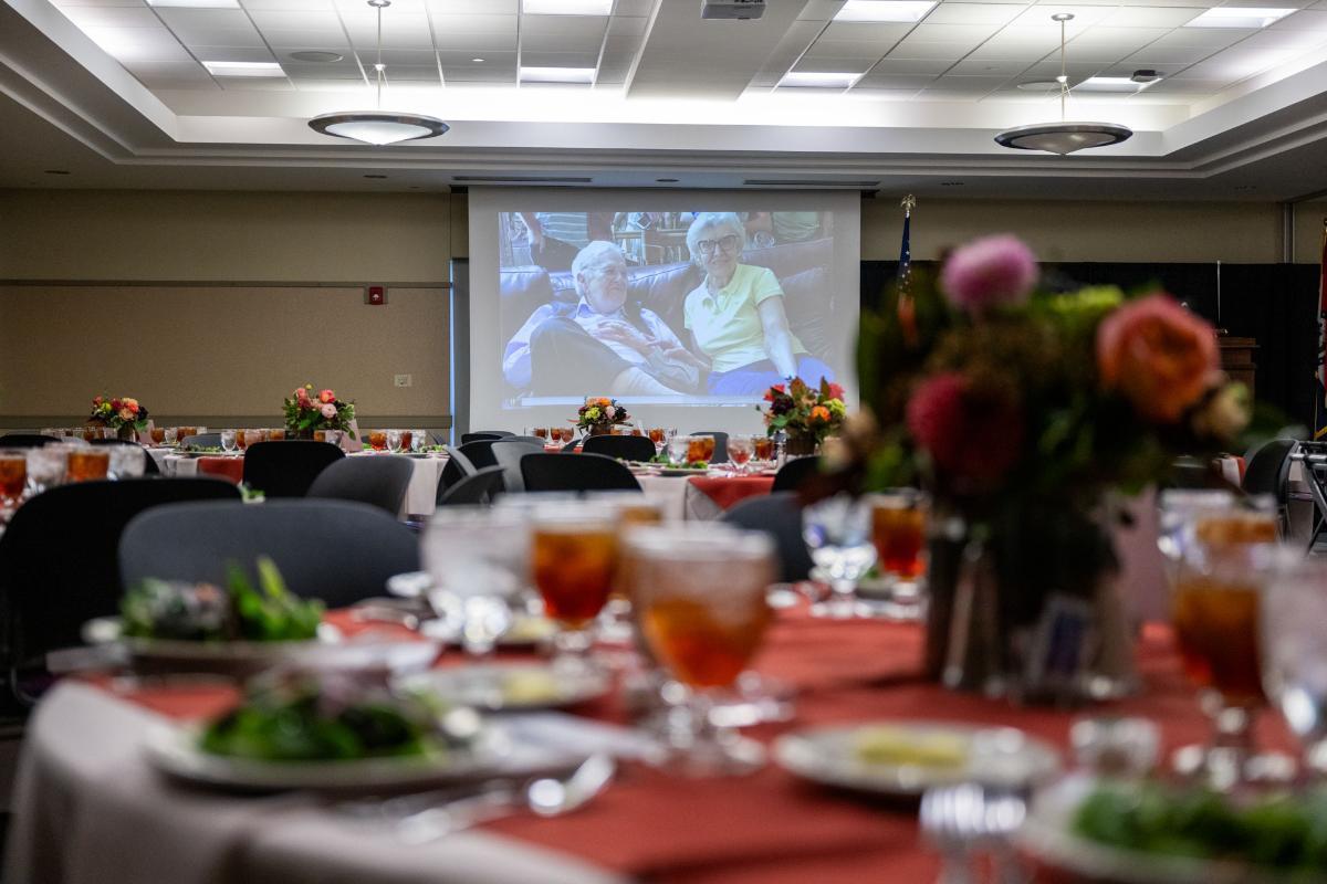 Conference room with round tables set for lunch and a projector image in the background.